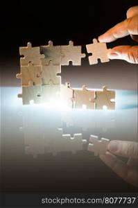 Wooden puzzle and backlight background. Vertically stacked parts. Hand holding puzzle piece.