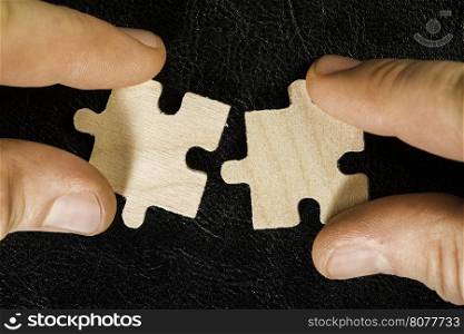 Wooden puzzle on black background. Hand holding puzzle piece.