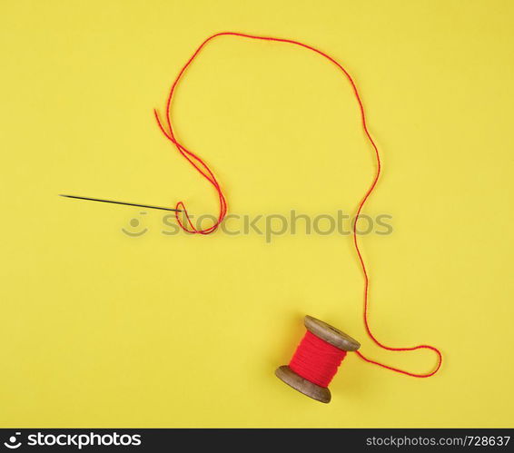 wooden reel with red wool thread and a large needle, yellow background, copy space