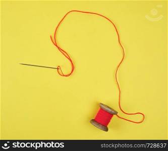 wooden reel with red wool thread and a large needle, yellow background, copy space