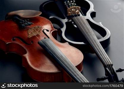 Wooden retro violin and modern electric viola, closeup view, nobody. Two classical string musical instruments, black background. Wooden retro violin and modern electric viola