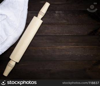 wooden rolling pin and a white textile towel on a brown wooden table, copy space. wooden rolling pin and a white textile towel