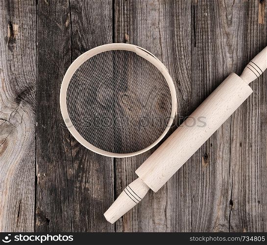 wooden rolling pin and a wooden round sieve on a gray table, top view