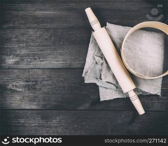 wooden rolling pin and round wooden sieve on a brown table, top view, copy space