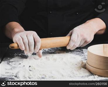 wooden rolling pin in men's hands, white wheat flour is poured on the table