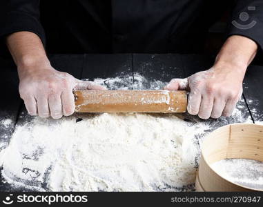 wooden rolling pin in men’s hands, white wheat flour is poured on the table