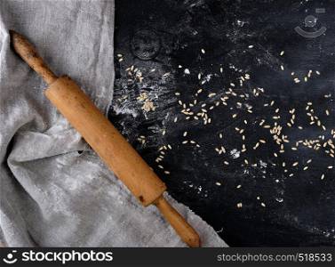 wooden rolling pin on a black background, near a gray linen towel, top view, sprinkled with flour and wheat, copy space