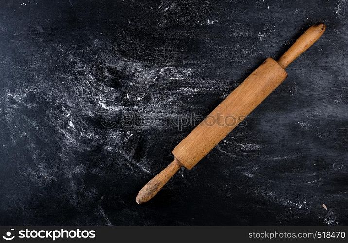 wooden rolling pin on a black background, white wheat flour, top view, copy space