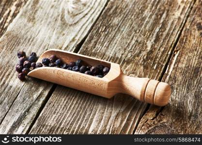 Wooden scoop with dried juniper berries over rustic background