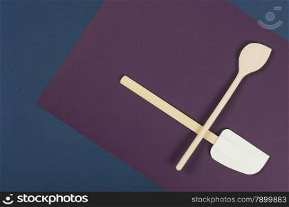 Wooden spatula and spoon arranged to overlap on a napkin over a blue background in a food preparation and baking concept, overhead view