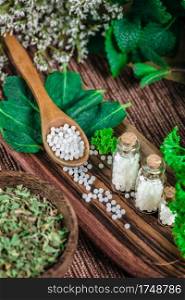 Wooden spoon full of homeopathic globules, small bottles with homeopathic pills and mint leaves in background