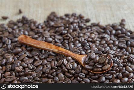 Wooden spoon on the background of roasted coffee beans, scattered on rough burlap