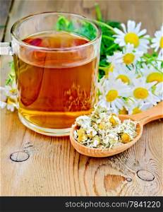 Wooden spoon with dried chamomile flowers, a bouquet of fresh flowers of chamomile tea in glass mug on the background of wooden boards