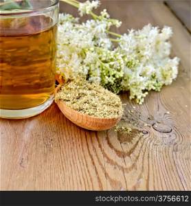 Wooden spoon with dried flowers, a bouquet of fresh flowers of meadowsweet, tea in glass mug on the wooden boards