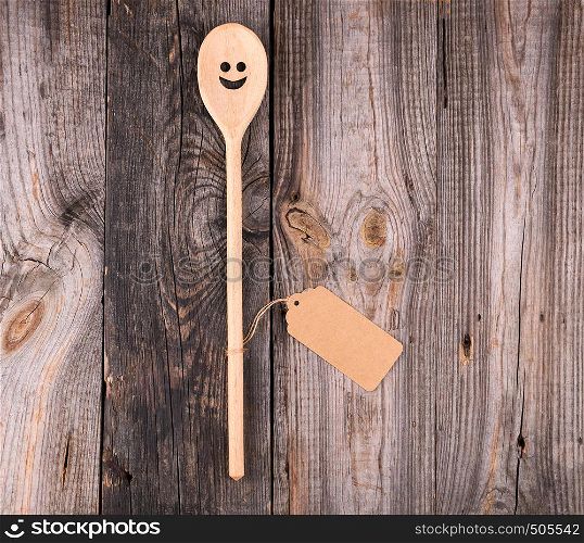 wooden spoon with embedded eyes and a smile, empty brown paper tag is attached to the handle with a rope, a gray wooden table