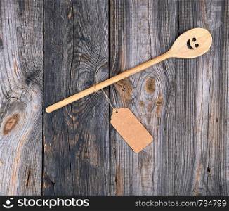wooden spoon with embedded eyes and a smile, empty brown paper tag is attached to the handle with a rope, a gray wooden table