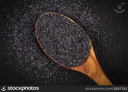 Wooden spoon with poppy seeds on dark stone background