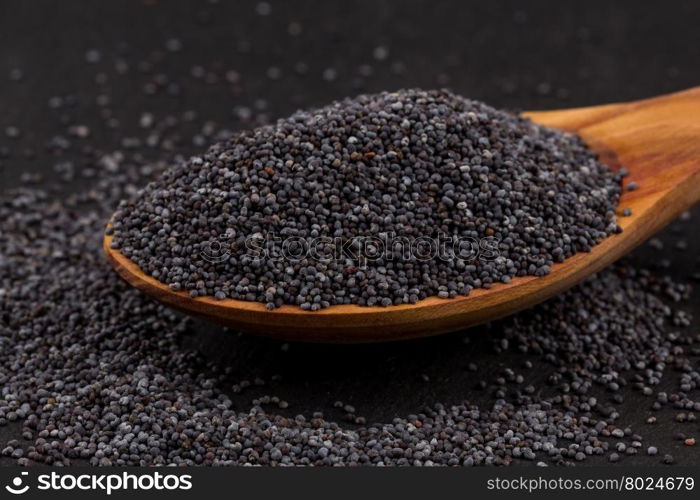 Wooden spoon with poppy seeds on dark stone background