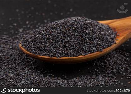 Wooden spoon with poppy seeds on dark stone background