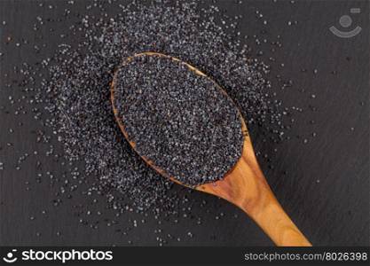 Wooden spoon with poppy seeds on dark stone background