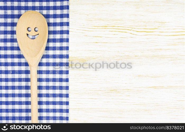 Wooden spoon with smile on blue checkered tablecloth on white wooden surface. Mockup for menu or recipe, restaurant, website with cooking. Kitchen food background, template, flat lay with copy space. Kitchen mockup. Wooden spoon with smile on white wooden background. Food background with copy space
