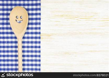 Wooden spoon with smile on blue checkered tablecloth on white wooden surface. Mockup for menu or recipe, restaurant, website with cooking. Kitchen food background, template, flat lay with copy space. Kitchen mockup. Wooden spoon with smile on white wooden background. Food background with copy space