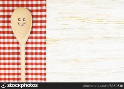 Wooden spoon with smile on red checkered tablecloth on white wooden surface. Mockup for menu or recipe, restaurant, website with cooking. Kitchen food background, template, flat lay with copy space. Kitchen mockup. Wooden spoon with smile on white wooden background. Food background with copy space