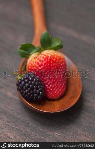 wooden spoon with strawberry and blackberry on a wooden surface