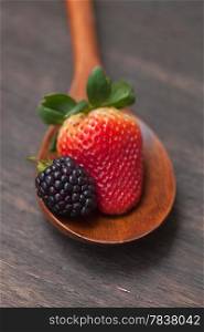 wooden spoon with strawberry and blackberry on a wooden surface