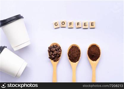 wooden spoons filled with coffee bean and crushed ground coffee , paper cup and coffee word on white background