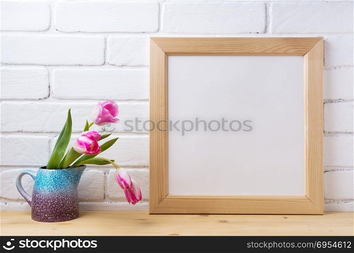Wooden square picture frame mockup with pink tulip in the purple blue pitcher vase. Empty frame mock up for presentation design. Template framing for modern art.