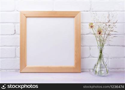 Wooden square picture frame mockup with wild grass in the glass jug. Empty frame mock up for presentation design. Template framing for modern art.