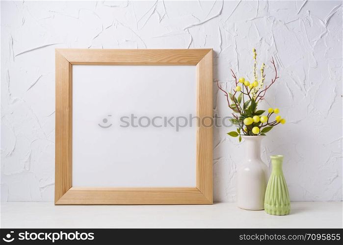 Wooden square picture frame mockup with yellow decorated branches and green vase. Empty frame mock up for presentation design. Template framing for modern art.