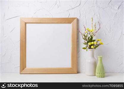 Wooden square picture frame mockup with yellow decorated branches and green vase. Empty frame mock up for presentation design. Template framing for modern art.