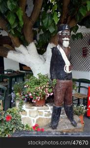 Wooden statue in uniform of a former Cretois on the front of a tree.