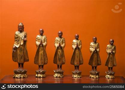Wooden statues of Buddha with five disciples against orange wall.