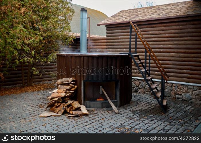 Wooden steaming bathtub with stove and ladder on outside terrace in yard. Spa and hygiene procedure. Wooden bathtub with stove on outside terrace
