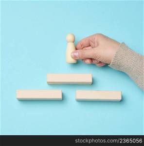 wooden steps and a figurine of a little man in a woman&rsquo;s hand. Startup, starting a new successful business, achieving goals