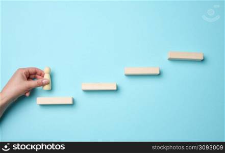 wooden steps and a figurine of a little man in a woman&rsquo;s hand. Startup, starting a new successful business, achieving goals
