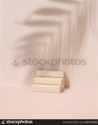 Wooden steps and shadow from a palm leaf on a beige background. Stage for demonstration and advertising of products, cosmetics, goods