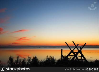 Wooden stile silhouette at sunset by a calm bay