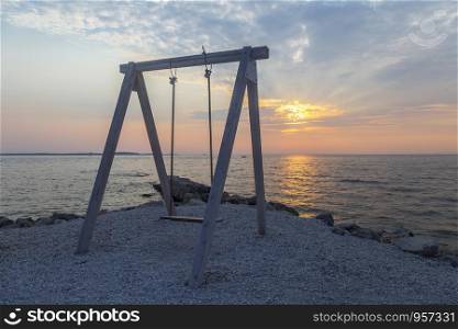 wooden swing chair near the sea on summer sunset