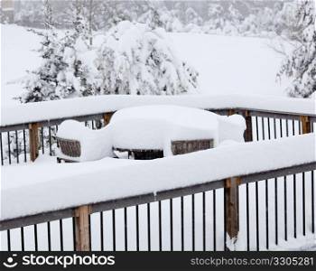 Wooden table and chairs buried deep in snow on deck after blizzard