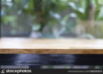 wooden table beside window with green leaves background for montage or display your product