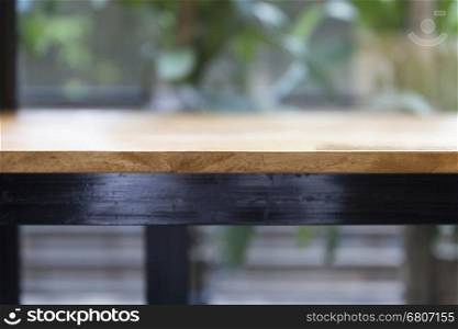 wooden table beside window with green leaves background for montage or display your product