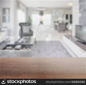 wooden table top with blur image of modern living room interior with dining table and pantry at home