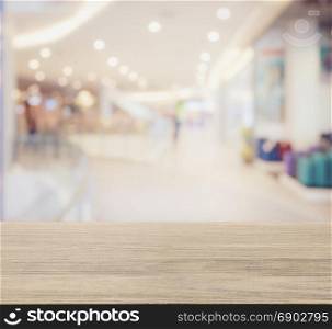 wooden table top with blur image of shopping mall interior with bokeh as background