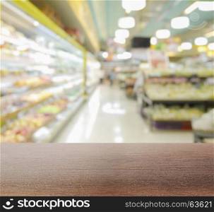 wooden table top with blur interior of supermarket with miscellaneous product on shelves