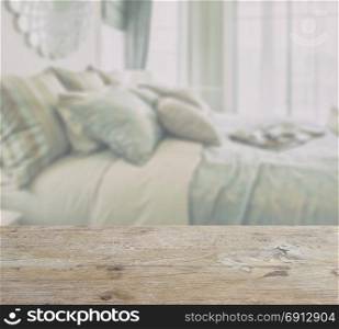 wooden table top with blur of bedroom interior with pillows and decorative set on the bed