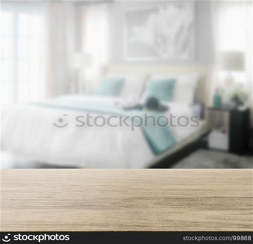 wooden table top with blur of cozy bedroom interior with white and green pillows on bed
